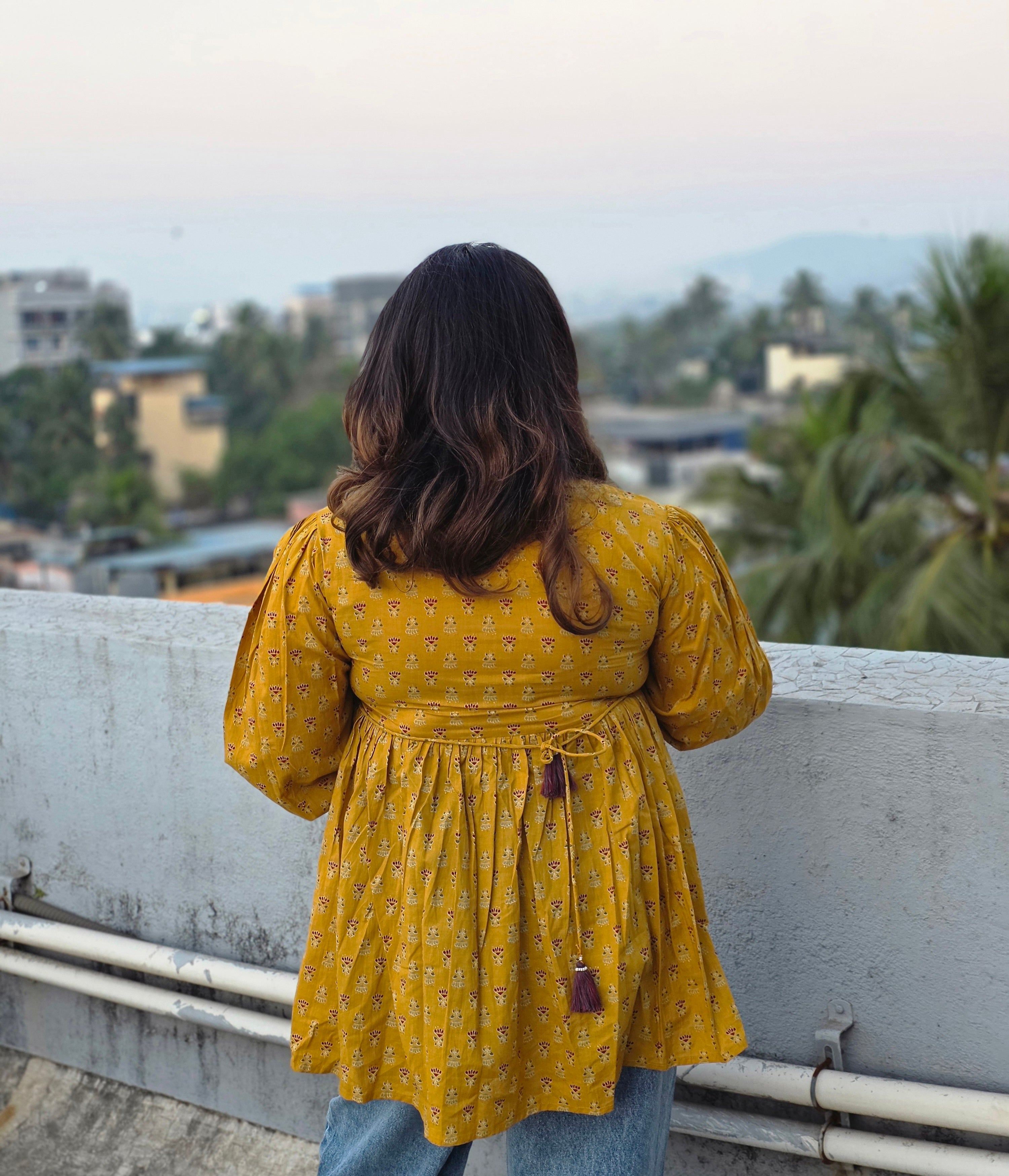 Person wearing a Sunheri Top standing on a balcony with a cityscape view.