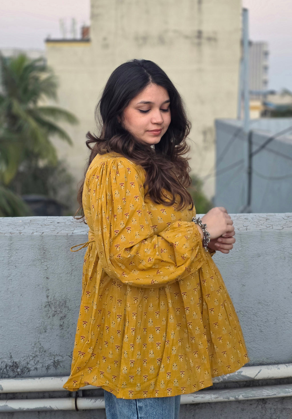 Woman in a Sunheri Top standing on a rooftop with buildings and trees in the background