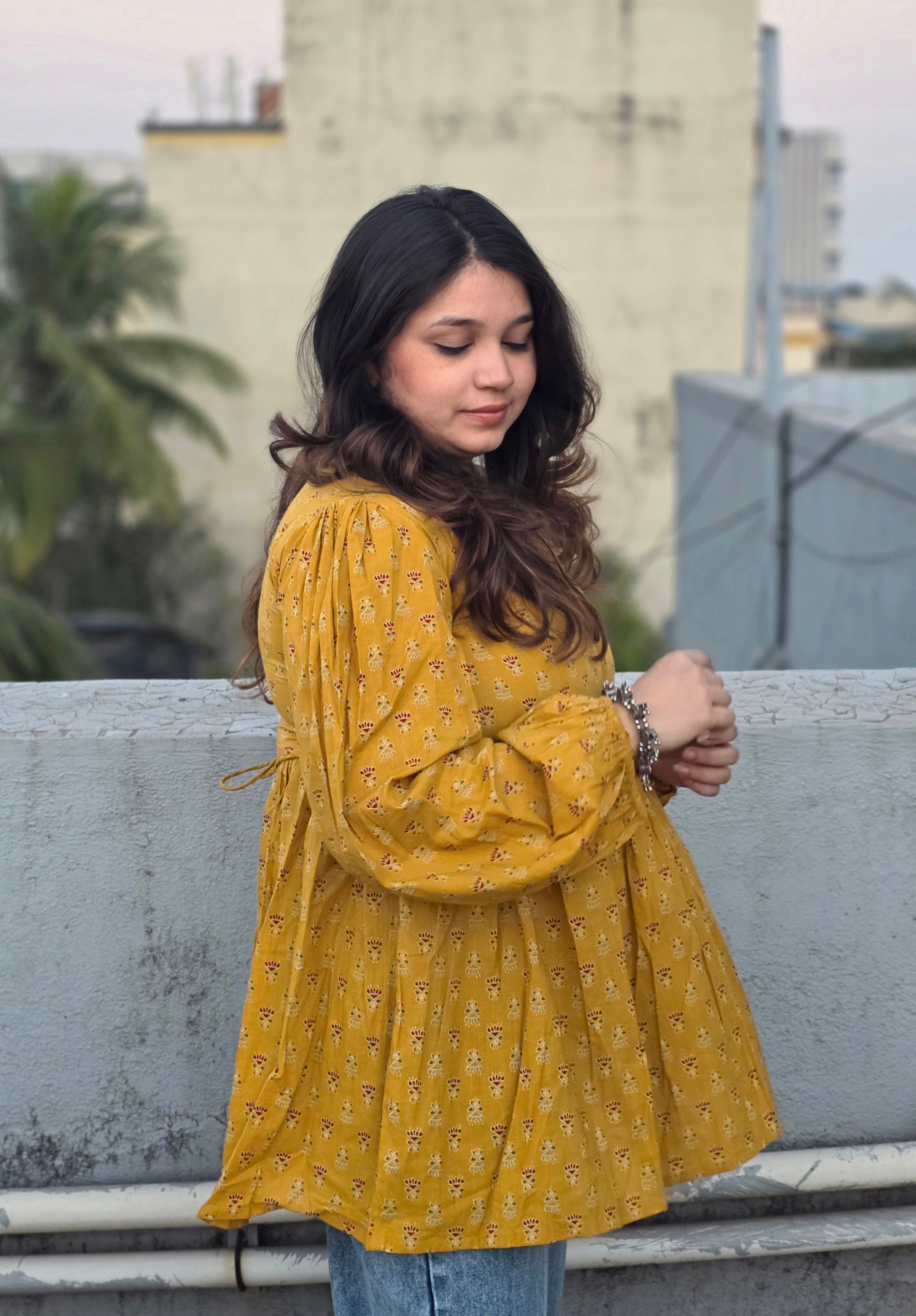 Woman in a Sunheri Top standing on a rooftop with buildings and trees in the background