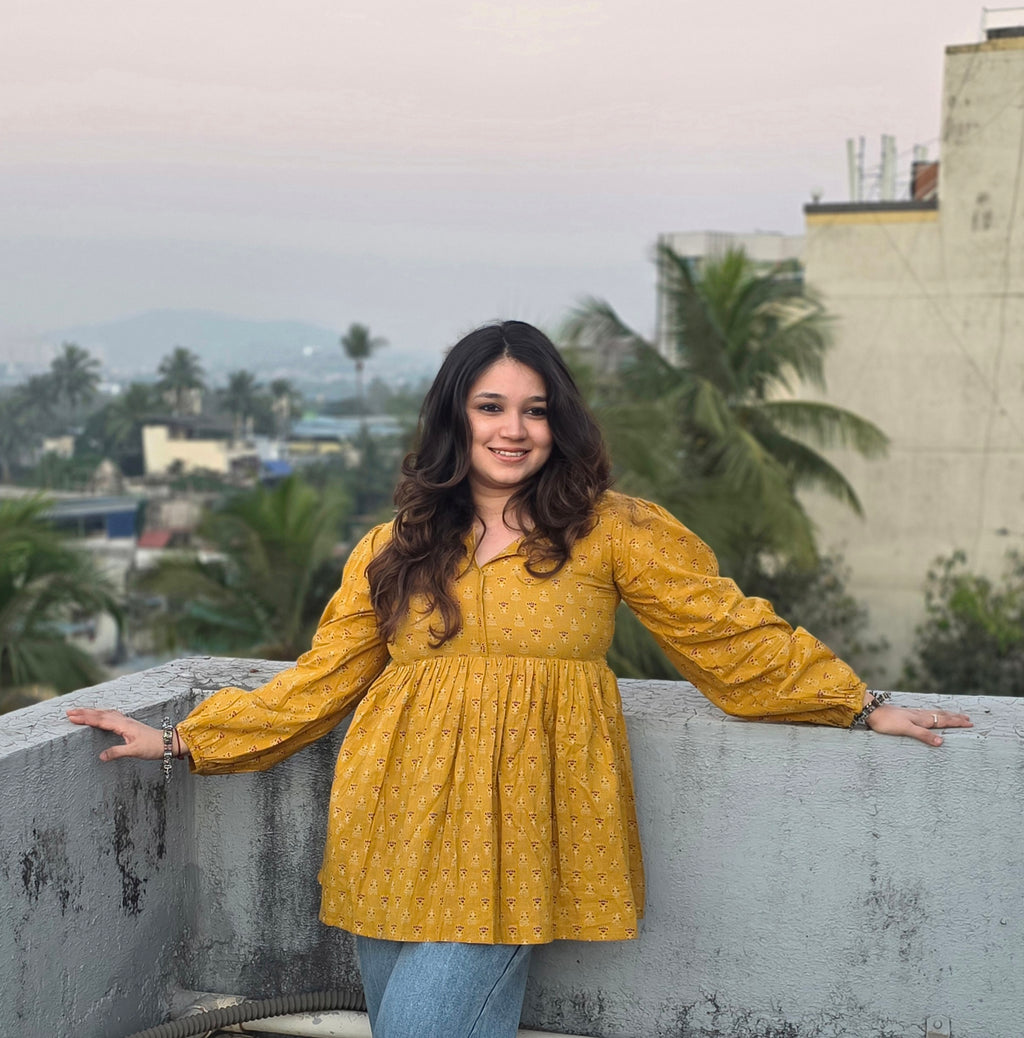 Woman in a Sunheri Top standing on a rooftop with palm trees and buildings in the background