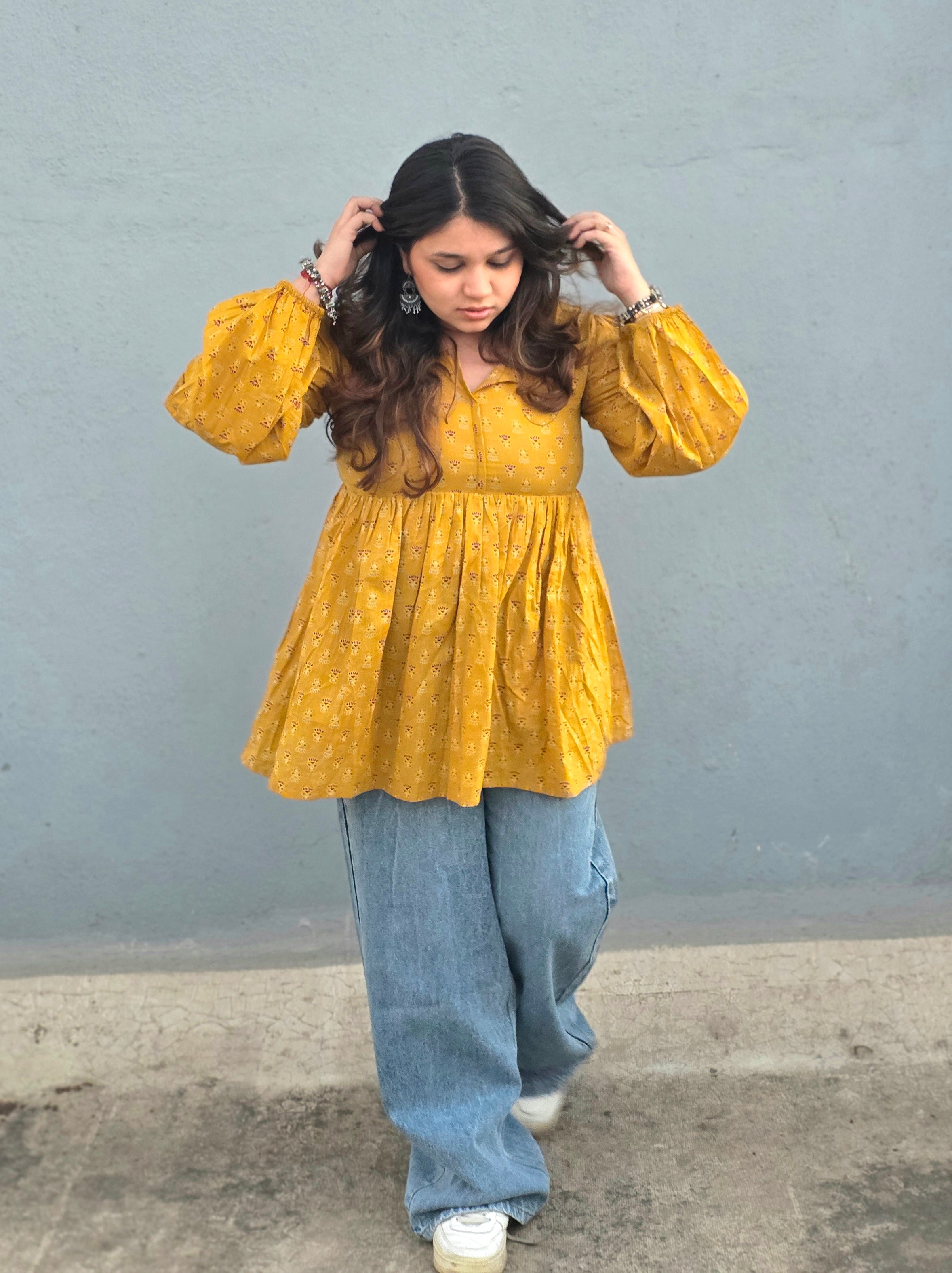 Woman wearing a Sunheri Top and blue jeans against a gray wall.