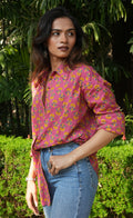 Woman wearing a Gulnaar shirt shirt and blue jeans standing outdoors with greenery in the background