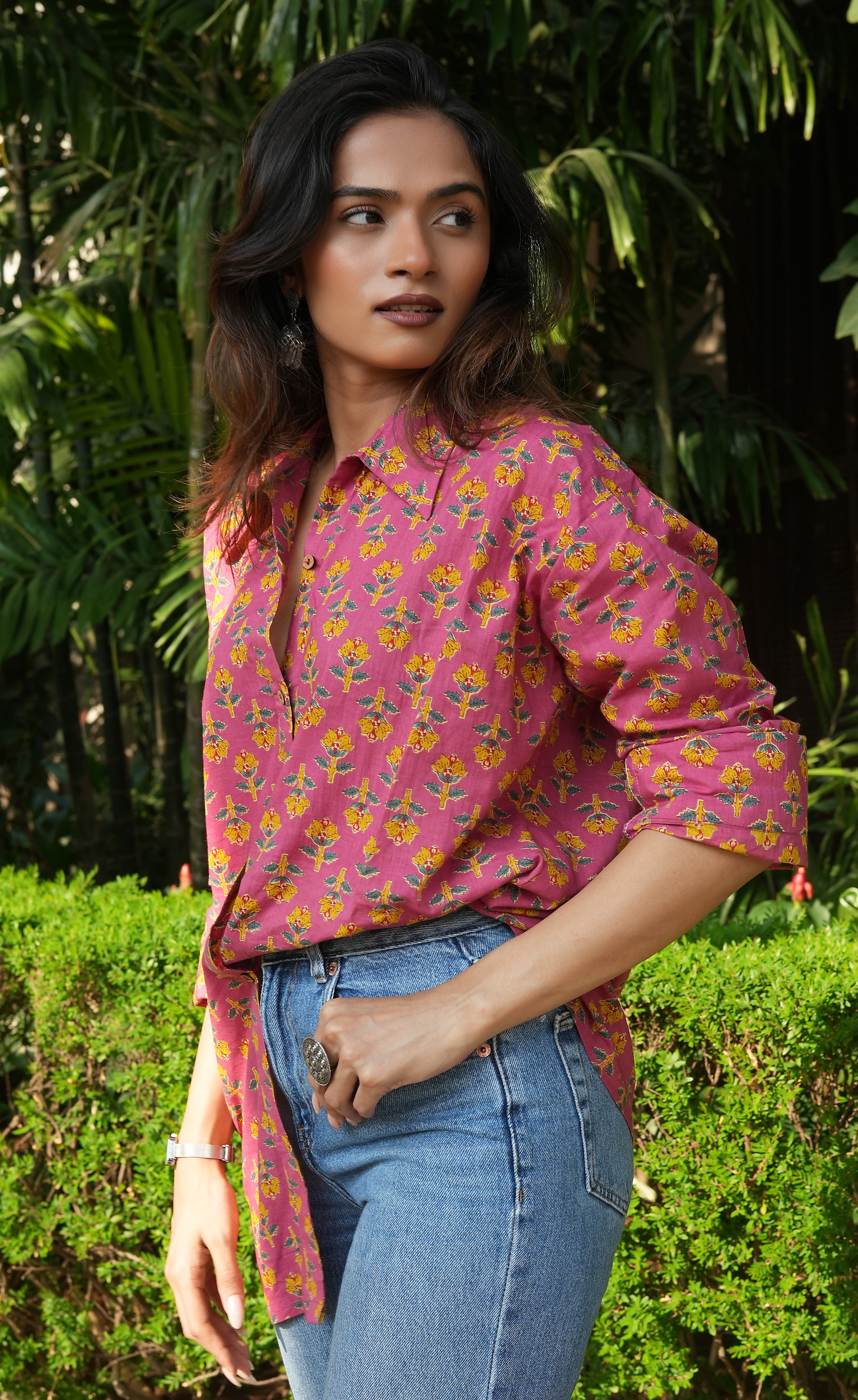 Woman wearing a Gulnaar shirt shirt and blue jeans standing outdoors with greenery in the background
