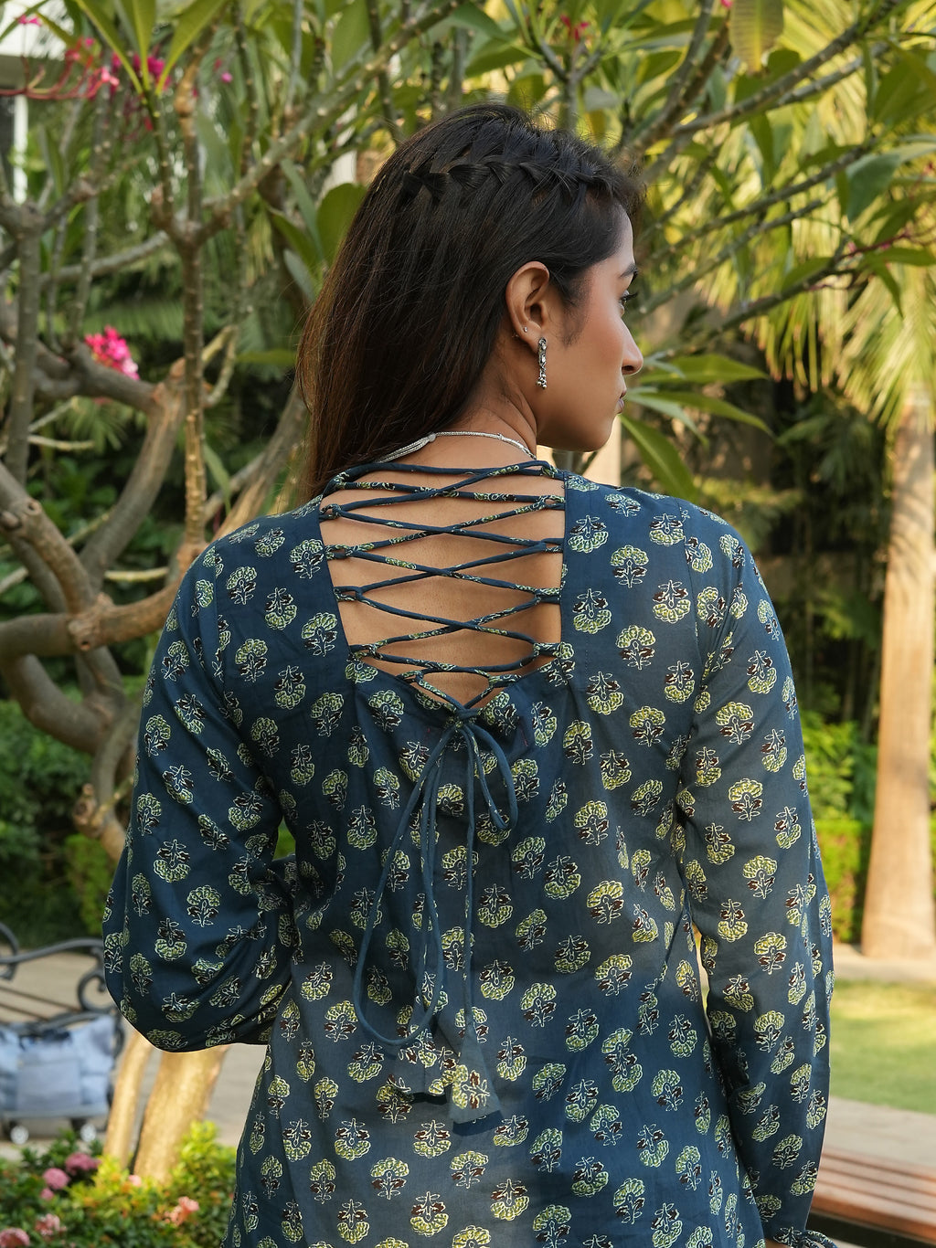 Woman wearing a blue patterned dress with a lace-up back in a garden setting