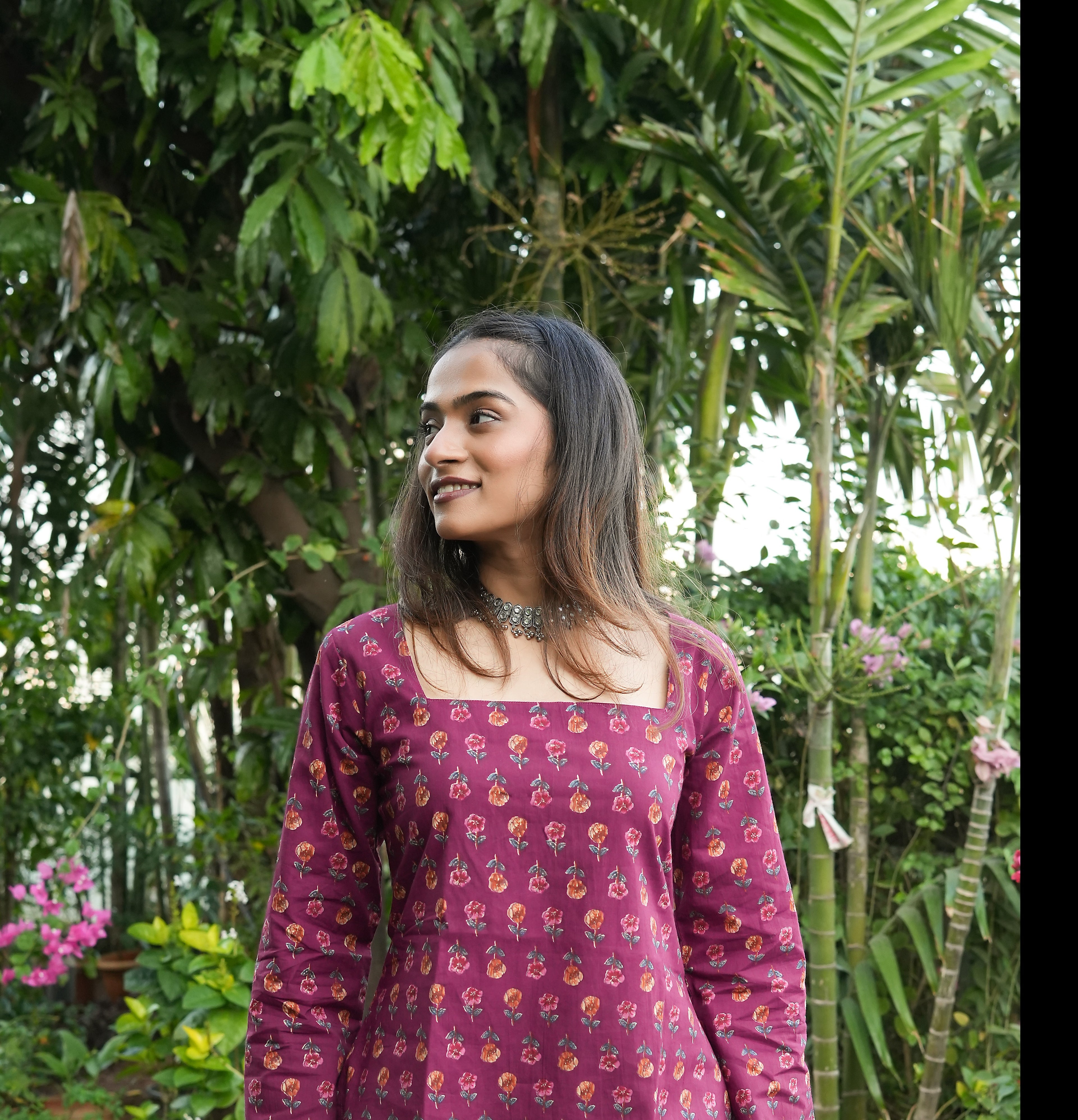 Woman wearing a patterned Wine blossom kurti dress standing in a garden with greenery.