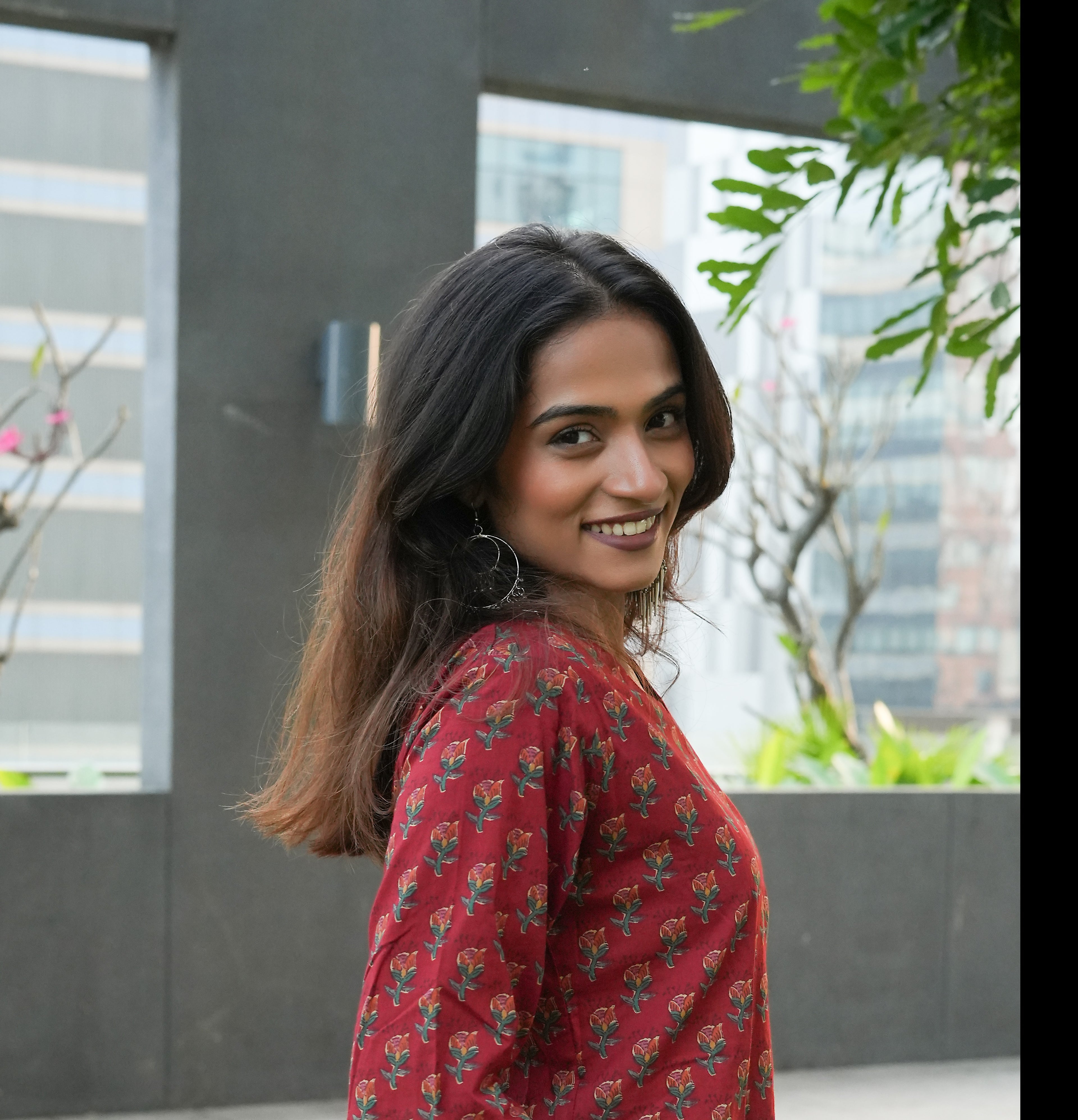 Woman in a Laal kurta standing outdoors with greenery and buildings in the background