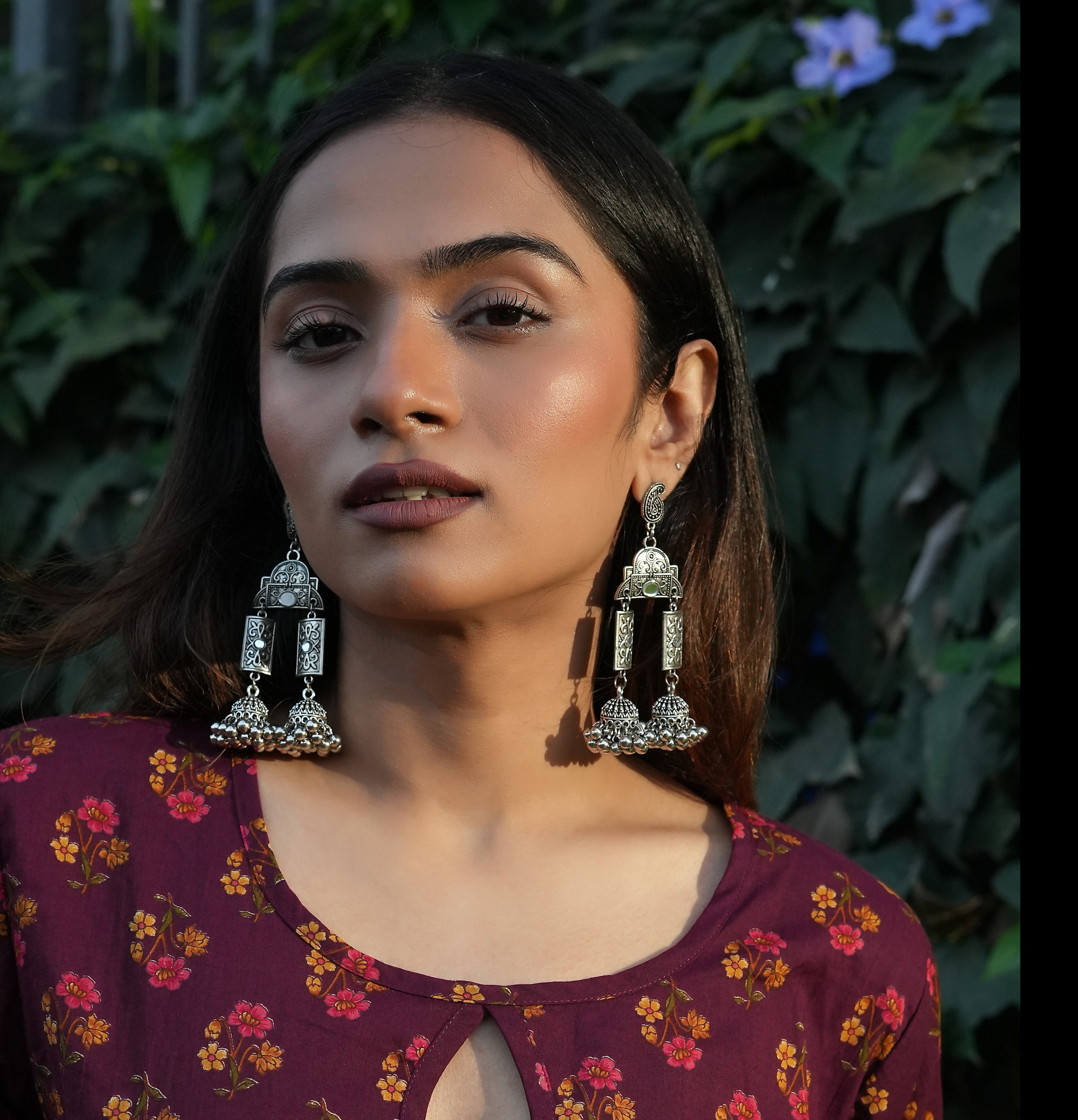Woman wearing large, oPlum bloom tie-up kurti against a green leafy background