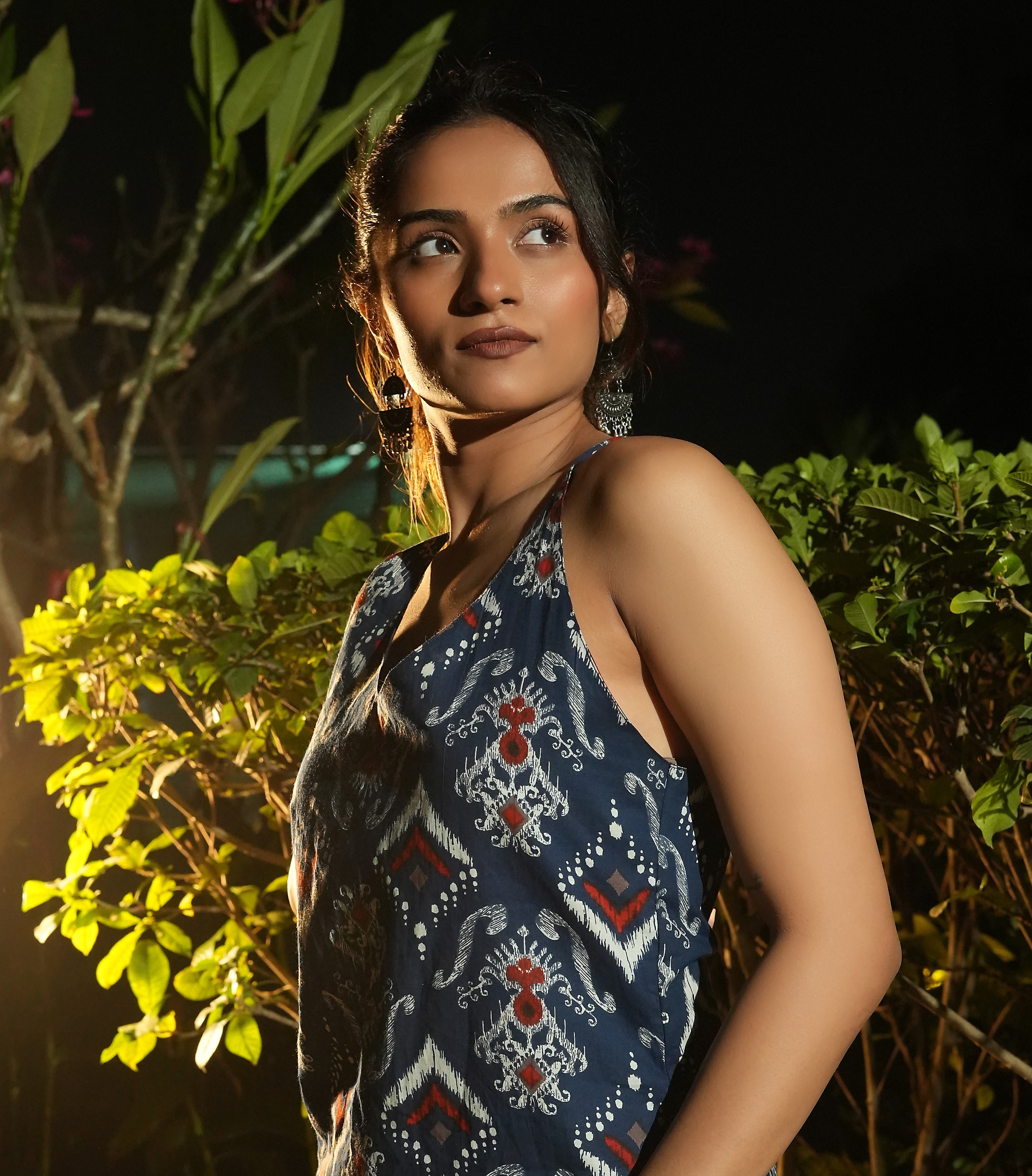 Woman wearing aNeel ikat kurta standing among green plants at night.
