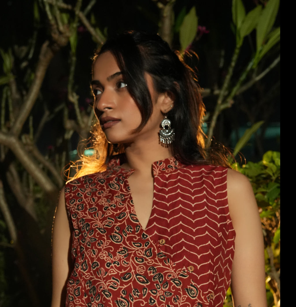 Woman wearing a Maroon overlap top with earrings against a dark background