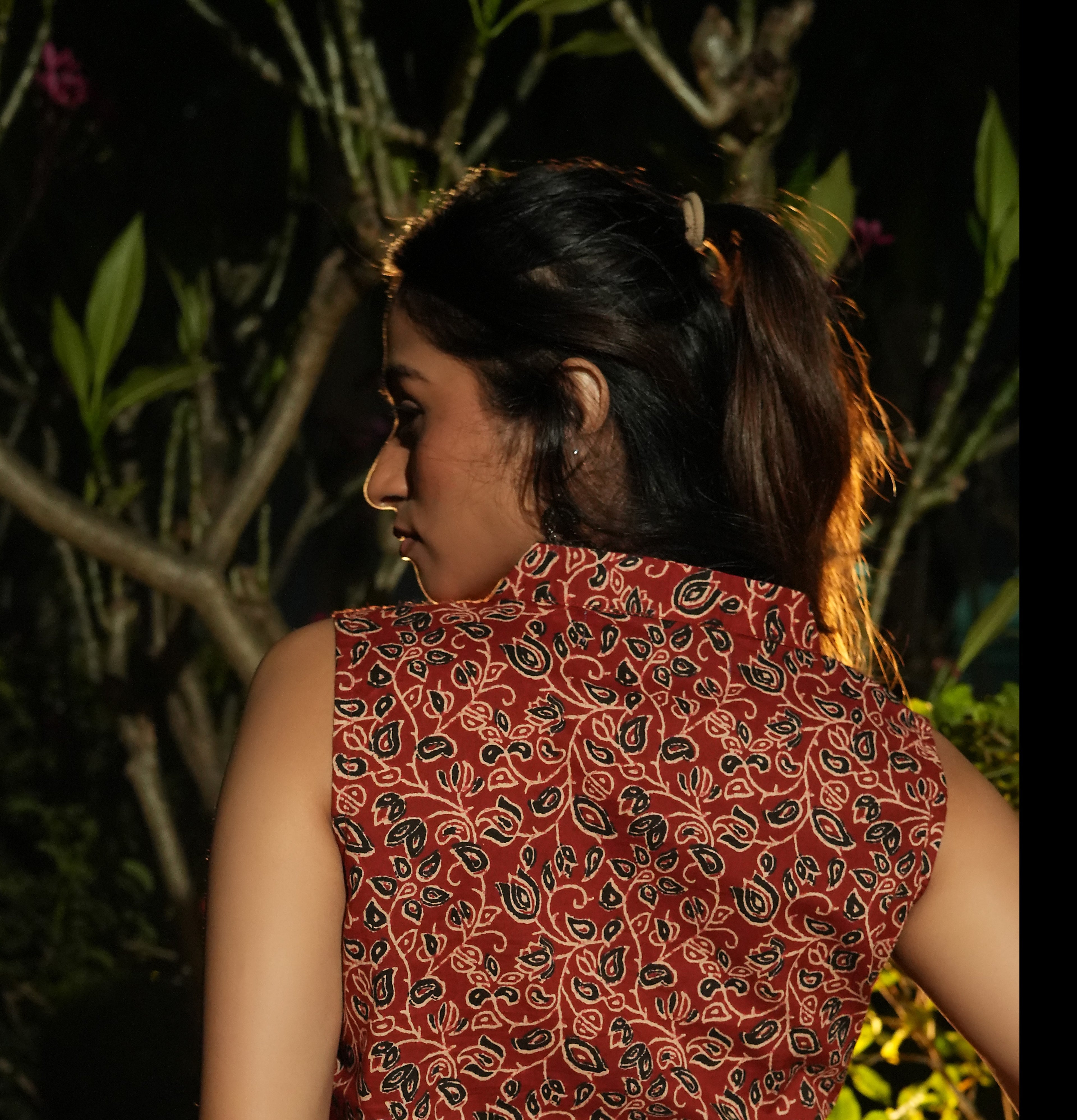 Woman wearing a Maroon overlap top with plants in the background