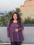 Woman wearing a Jamuni  Top standing on a rooftop with palm trees and buildings in the background.