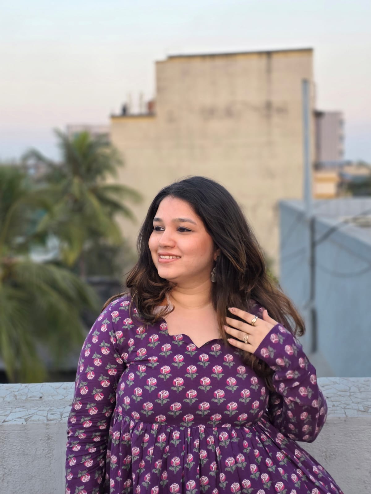 Woman in a Jamuni  Top standing on a rooftop with buildings and trees in the background