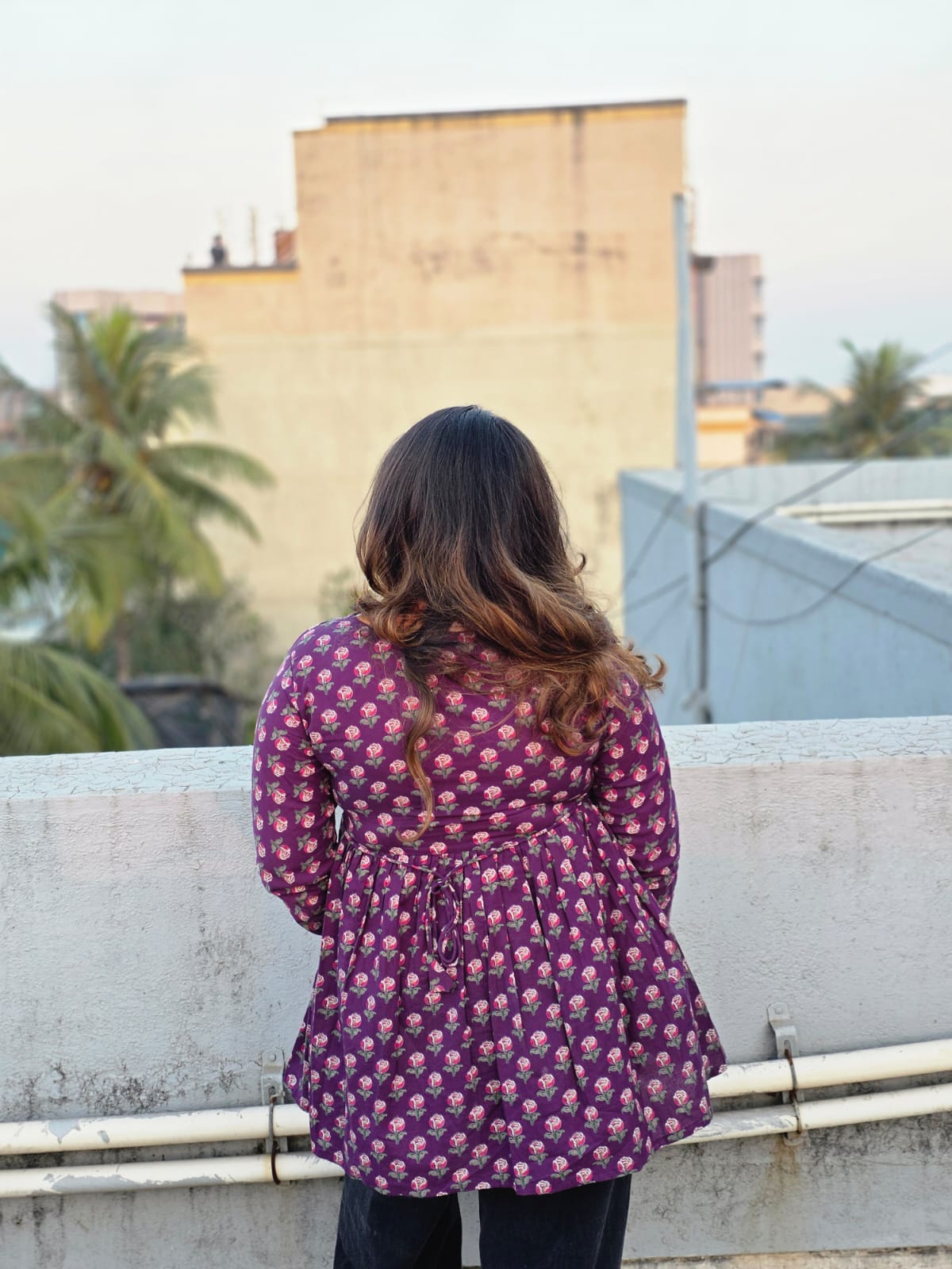 Person wearing a Jamuni Top standing on a rooftop with buildings and trees in the background