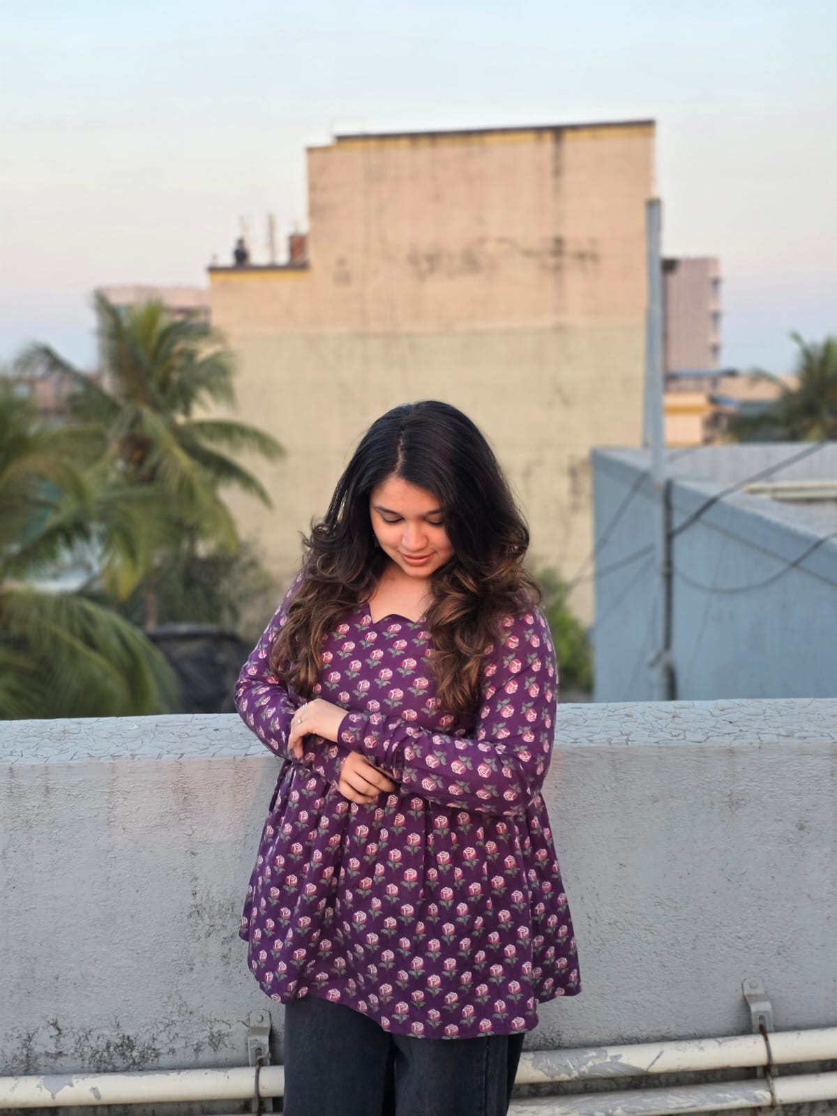 Woman wearing a Jamuni Top dress on a rooftop with buildings and trees in the background
